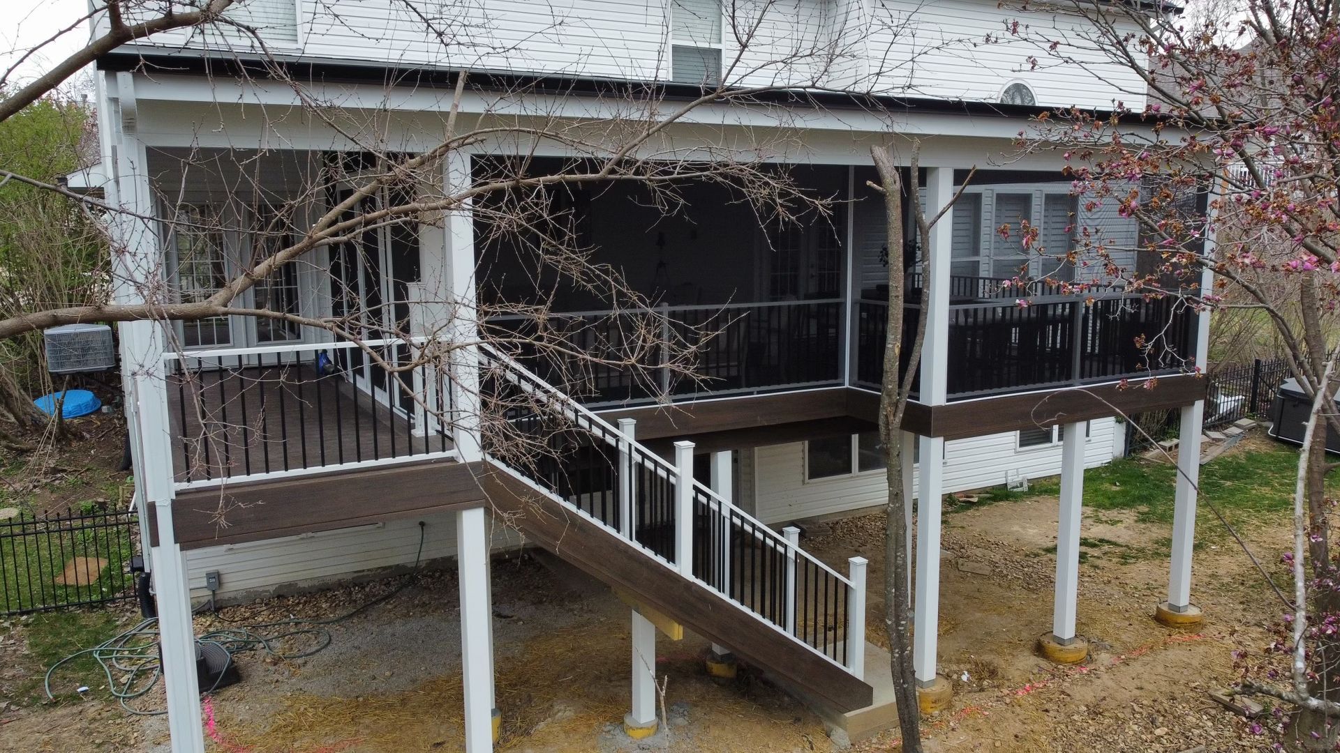 A two-story white house with a screened porch and brown deck. Staircase leads down.