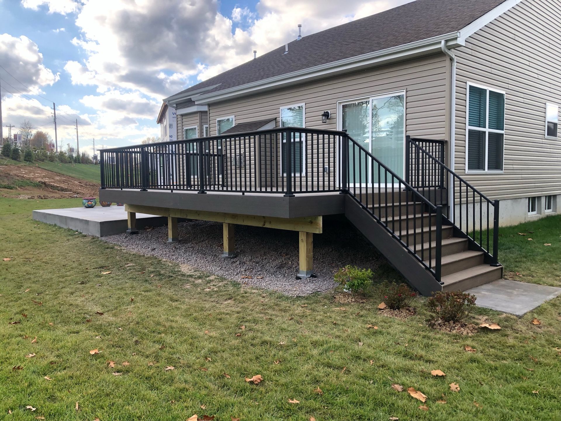 Backyard deck with black railing and stairs leading to a sliding glass door. Gray siding, grass, and gravel present.