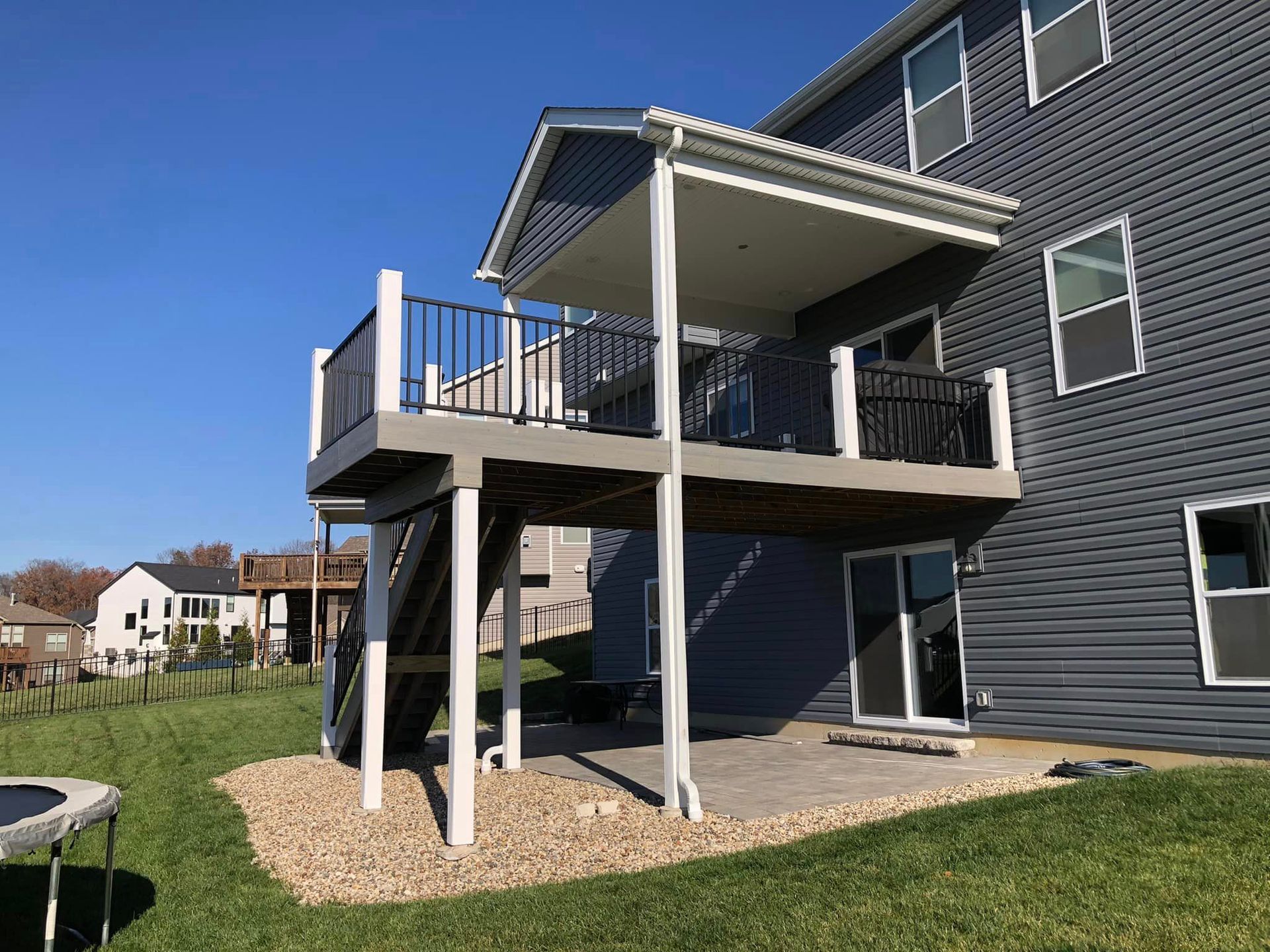 Two-story deck attached to a gray house, with black railings, white posts, and a covered upper level.