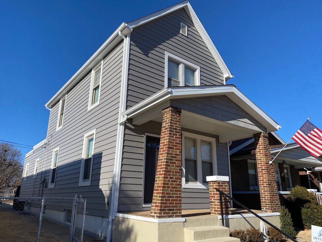 Two-story house with gray siding, white trim, and brick pillars. Blue sky background.