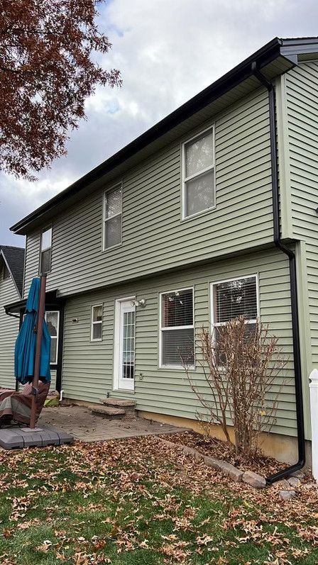 Two-story house with light green siding and black gutters, surrounded by a yard with brown leaves.