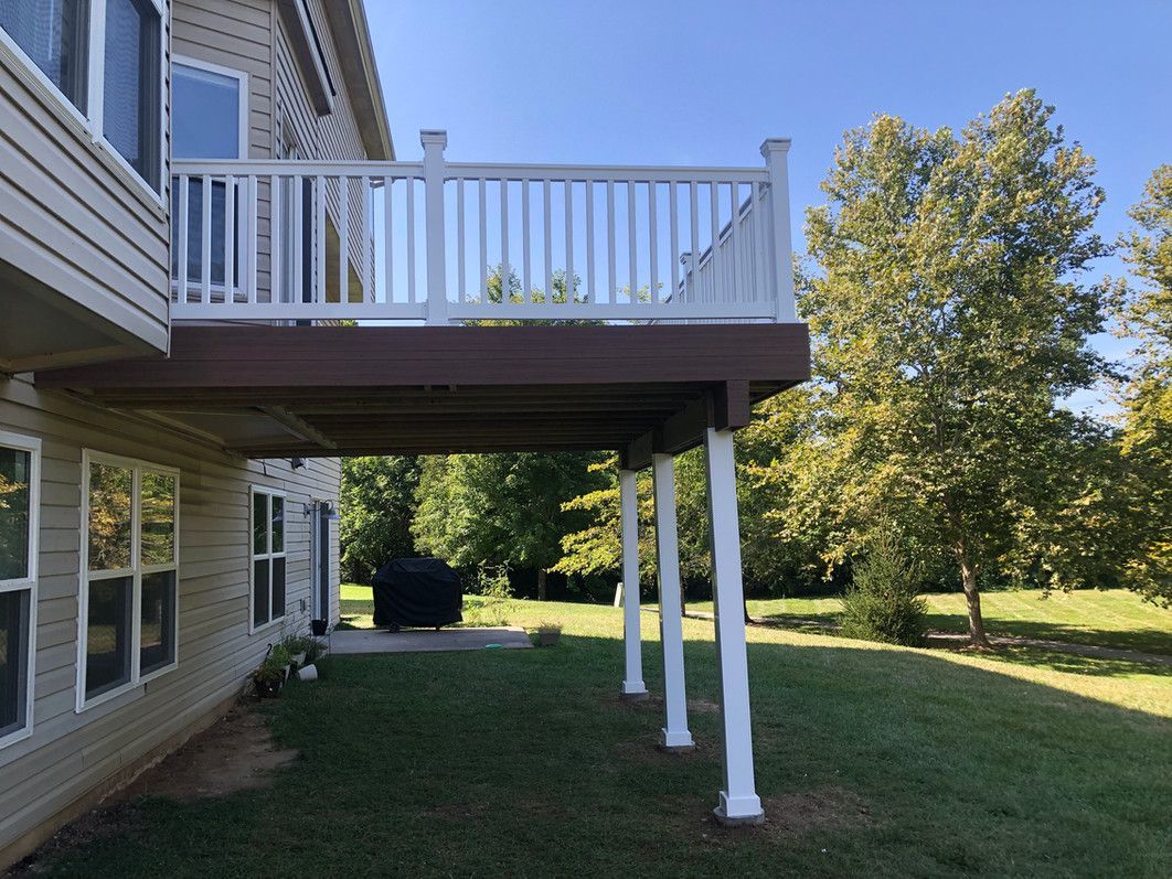 A two-story house with a wooden deck supported by white pillars. Backyard with green grass and trees.