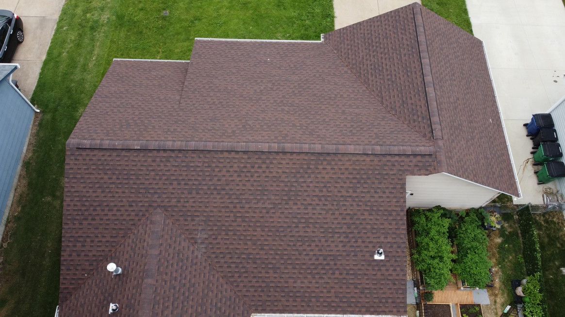 Overhead view of a brown shingled roof on a residential home with a green lawn.