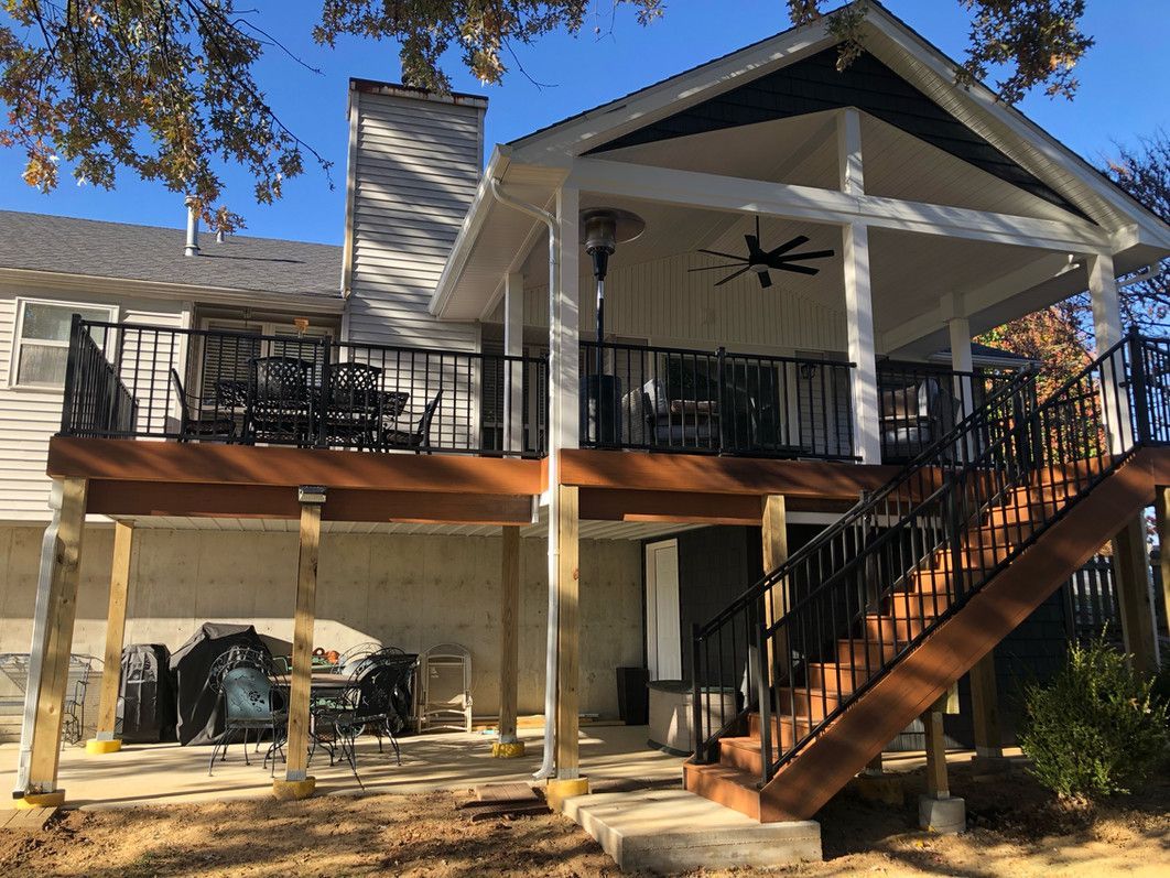 Deck with stairs, covered porch, and black railing. House exterior with a chimney.