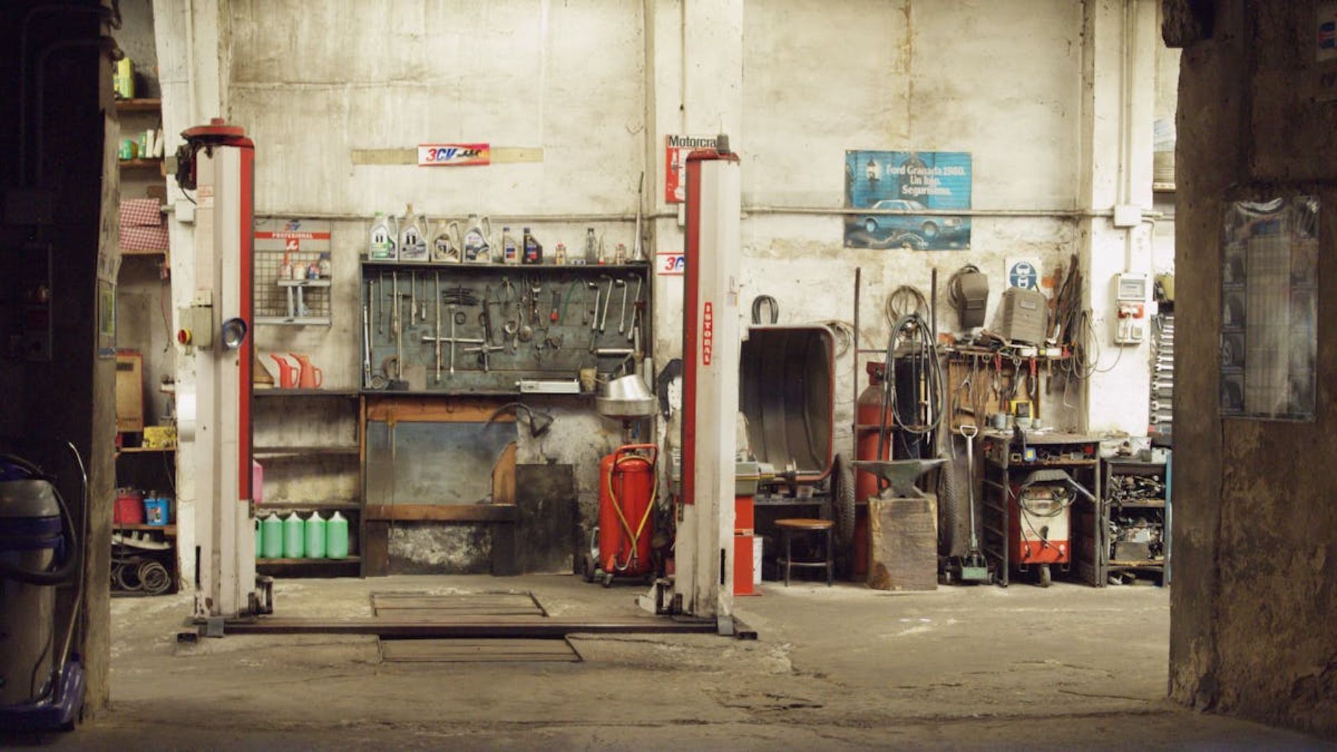 Interior de un taller de reparación de automóviles con elevadores de coches, herramientas y equipos industriales contra paredes de hormigón desgastadas.