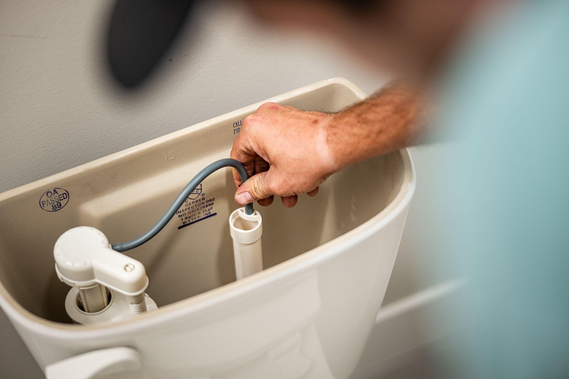 Hand adjusting a toilet tank fill valve with a blue hose inside an open toilet tank