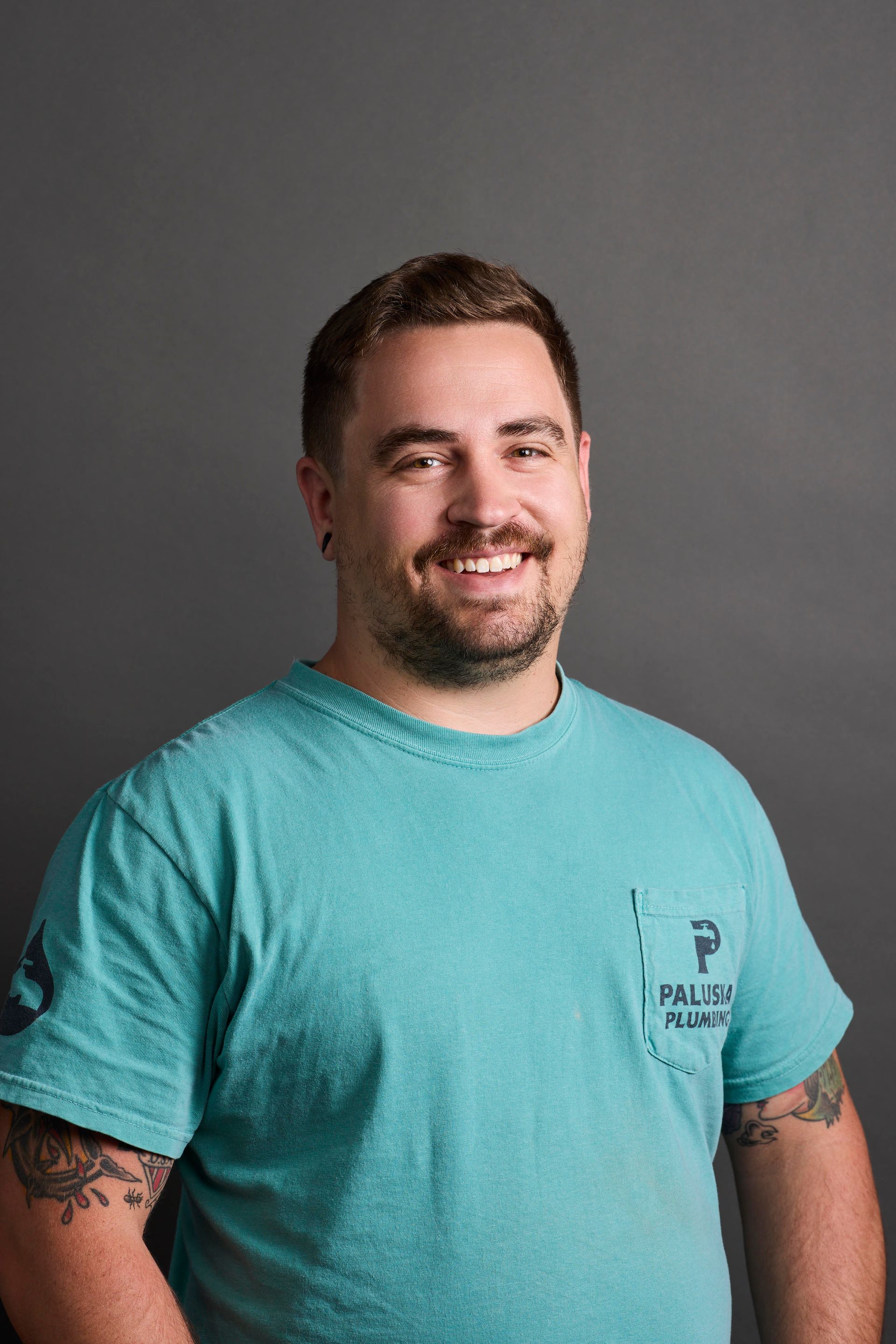 Smiling man in a teal T-shirt standing against a gray studio backdrop