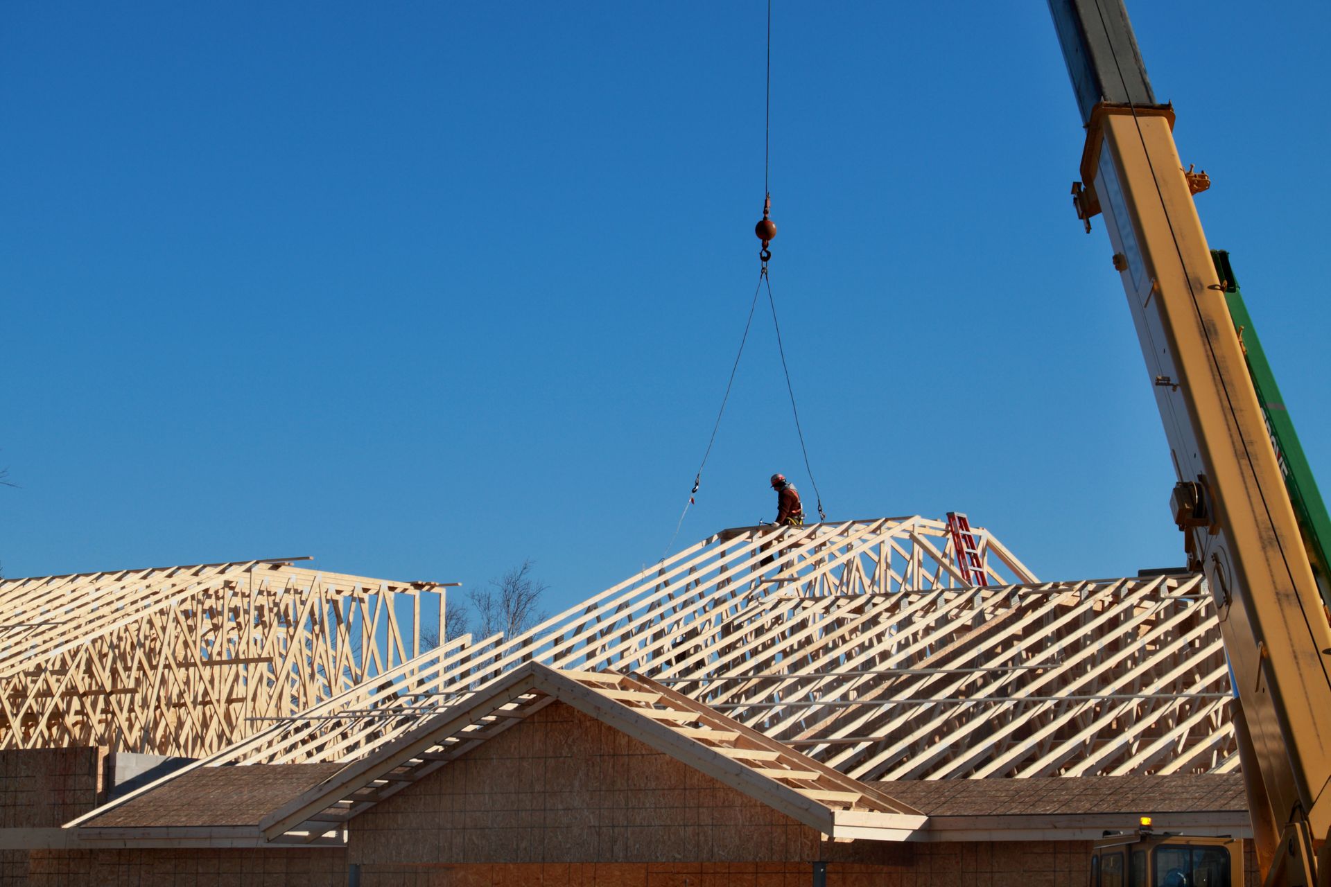 Crane lifting a roof truss at a house construction site. Crane lifting a roof truss at a house construction site.