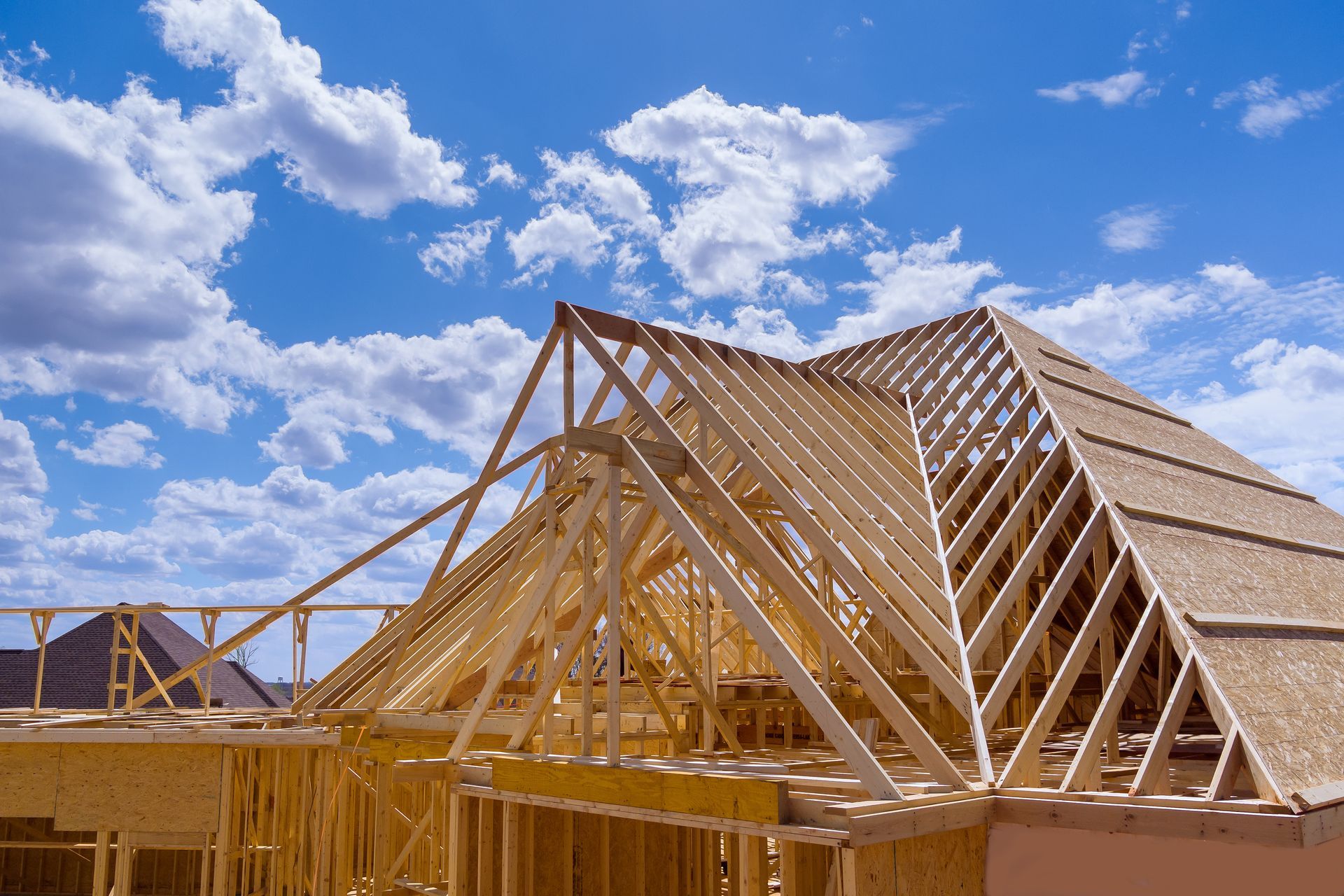 Wooden roof framing under construction on a house with blue sky and clouds. Wooden roof framing under construction on a house with blue sky and clouds.