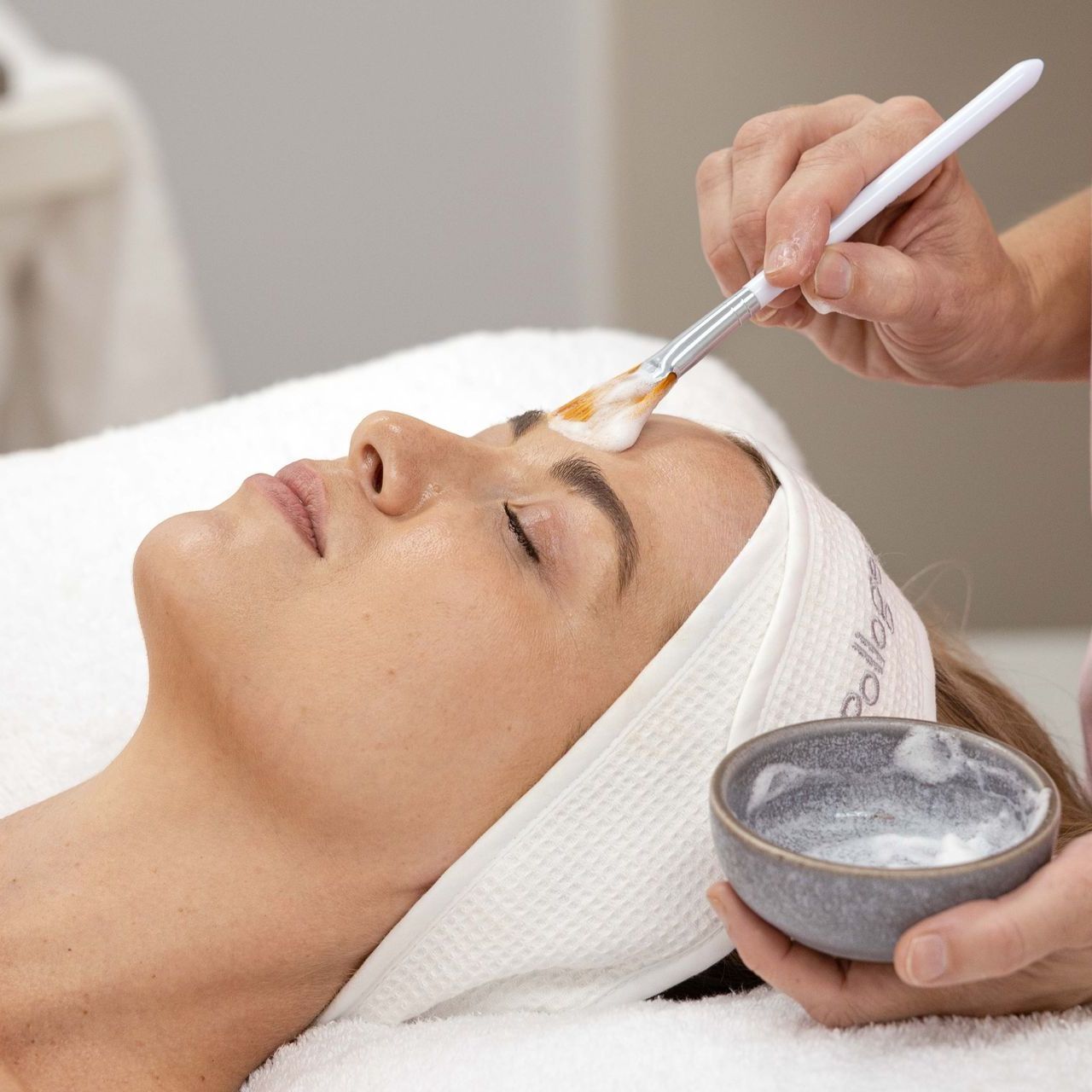A woman is getting a spray on her face at a spa.