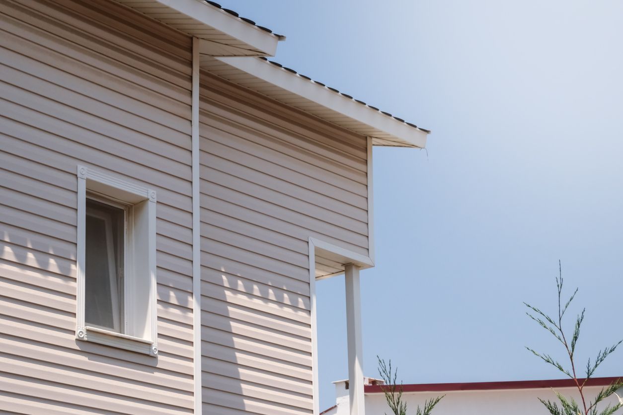 White house siding and roof eaves against a blue sky with a few small tree branches