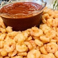 Bowl of red dipping sauce beside a pile of golden fried shrimp or fritters
