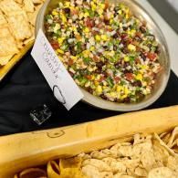 Bowl of colorful chopped salad beside tortilla chips on a buffet table