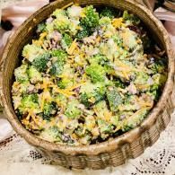 Basket of colorful salad with broccoli, shredded cheese, and herbs on a tablecloth
