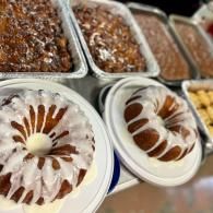 Assorted pastries in trays, including iced ring cakes with white and brown drizzle in the foreground.