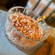 Clear glass cup with a pink, crumbly dessert topped with crushed nuts and a spoon