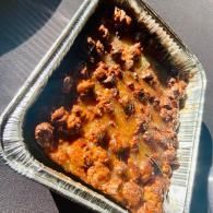 Takeout tray of baked pasta with browned cheese, viewed at an angle on a table