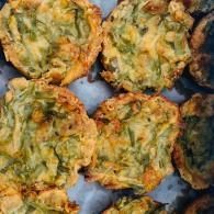 Golden-brown fritters with green herbs, arranged closely on a tray