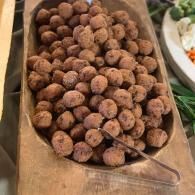 Tray of small brown dessert balls in a wooden serving dish with tongs at a buffet.