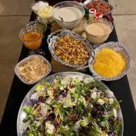 Salad bar with bowls of toppings, dressings, and a large mixed green salad on a countertop