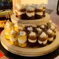 Tiered display of layered dessert cups with cream, chocolate, and yellow layers in a buffet setting
