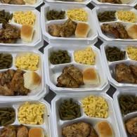 Rows of takeout meal boxes with chicken, green beans, yellow rice, and a dinner roll.