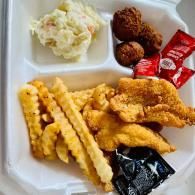 Takeout tray with fried chicken tenders, crinkle fries, mashed potatoes, and condiment packets