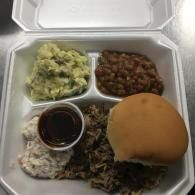 Takeout meal with mashed potatoes, baked beans, rice and meat, coleslaw, sauce, and a bread roll.