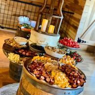 Wooden bowls of mixed snacks and fruit arranged on a tiered buffet table in a rustic indoor setting