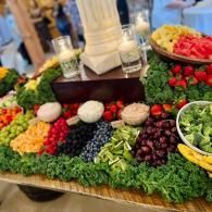 Fresh fruit and vegetable display on a buffet table with strawberries, grapes, kiwi, pineapple, and greens