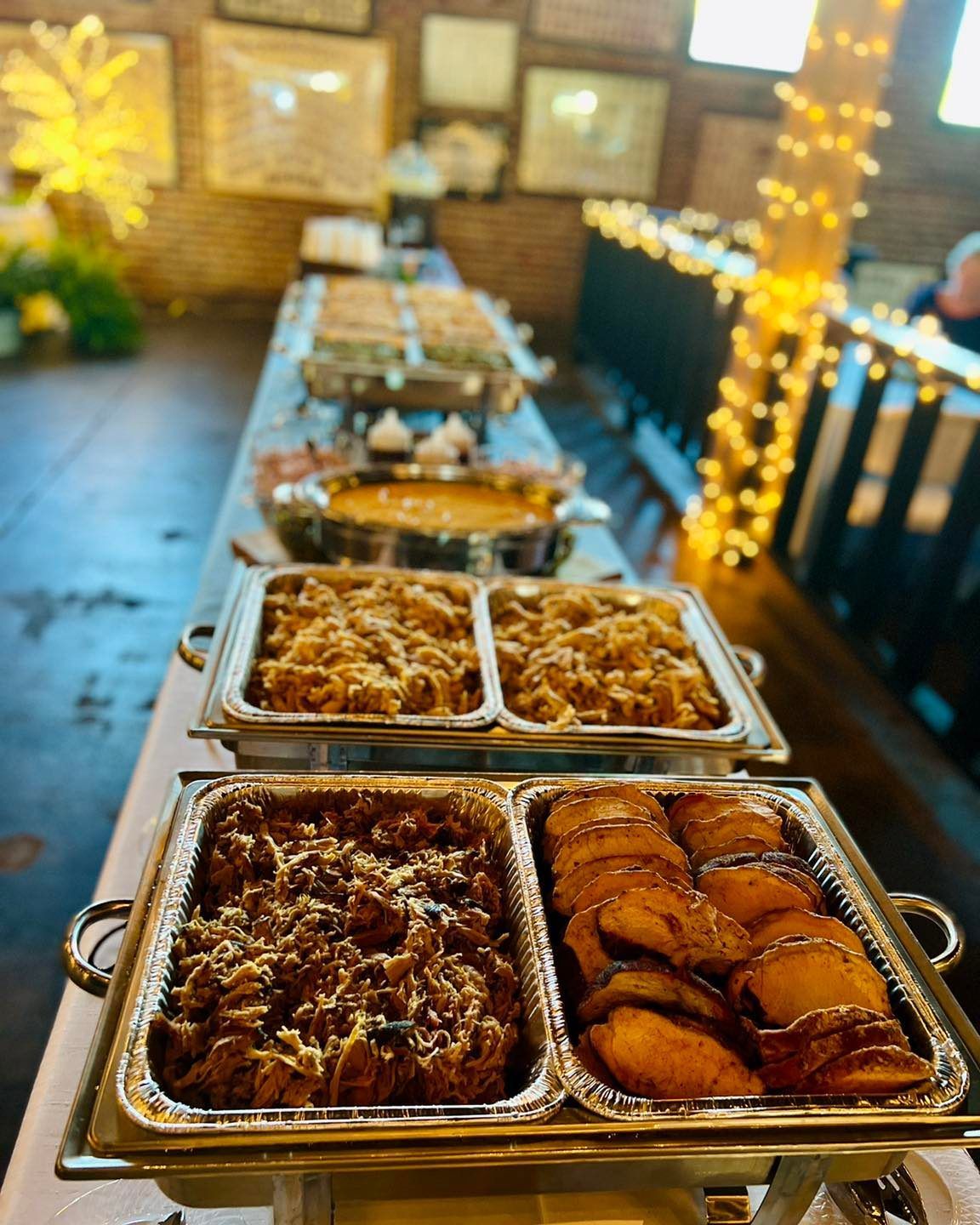 Buffet trays of baked dishes on a table with warm string lights in the background