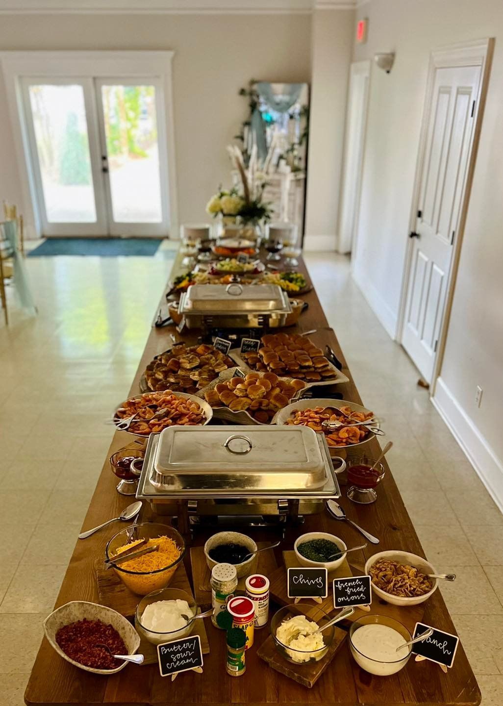 Long buffet table with covered dishes and condiments in a bright hallway
