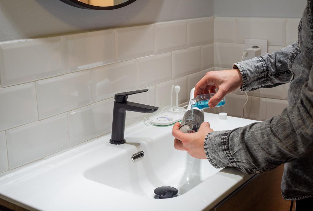 Man filling water flosser tank with mouthwash at bathroom sink