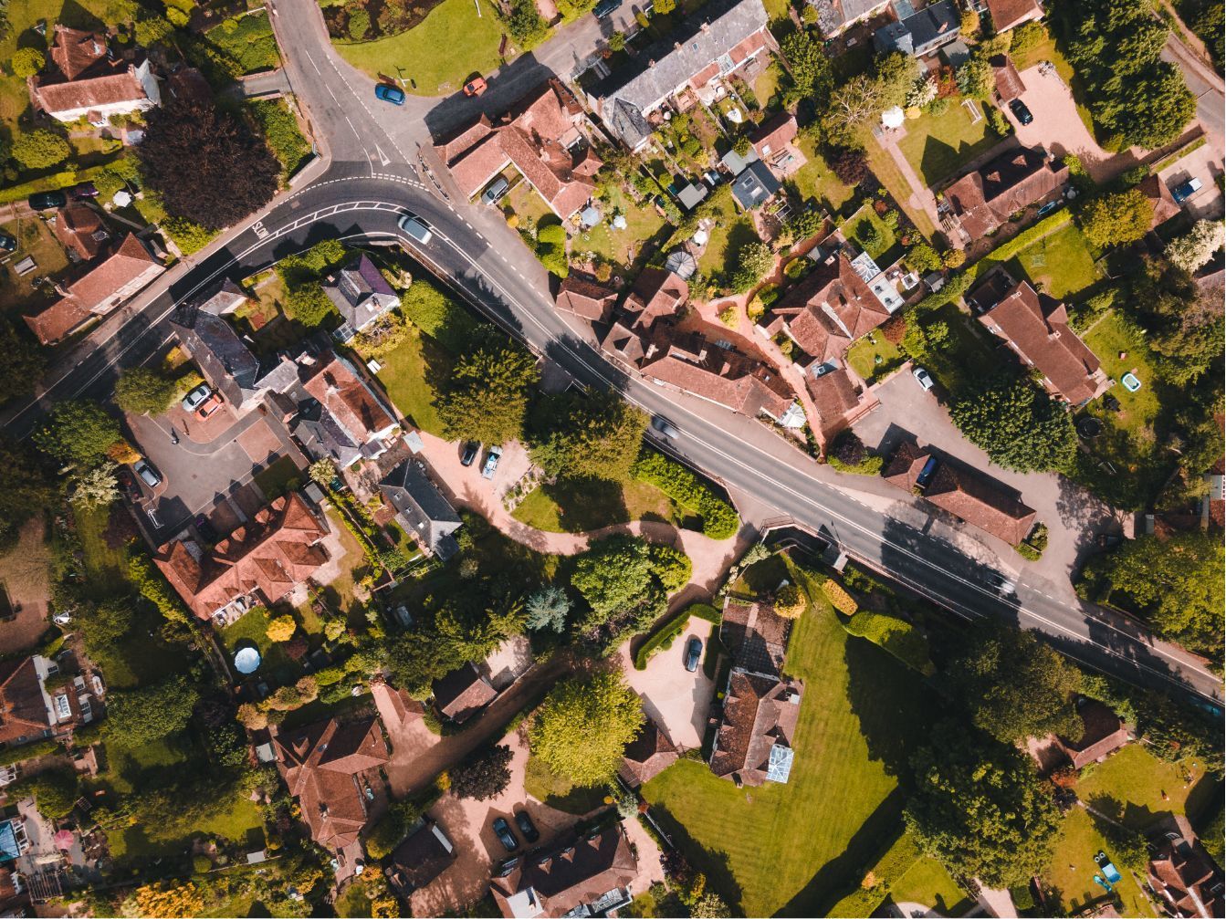 An aerial view of a residential neighborhood with several houses, trees, and a winding road.