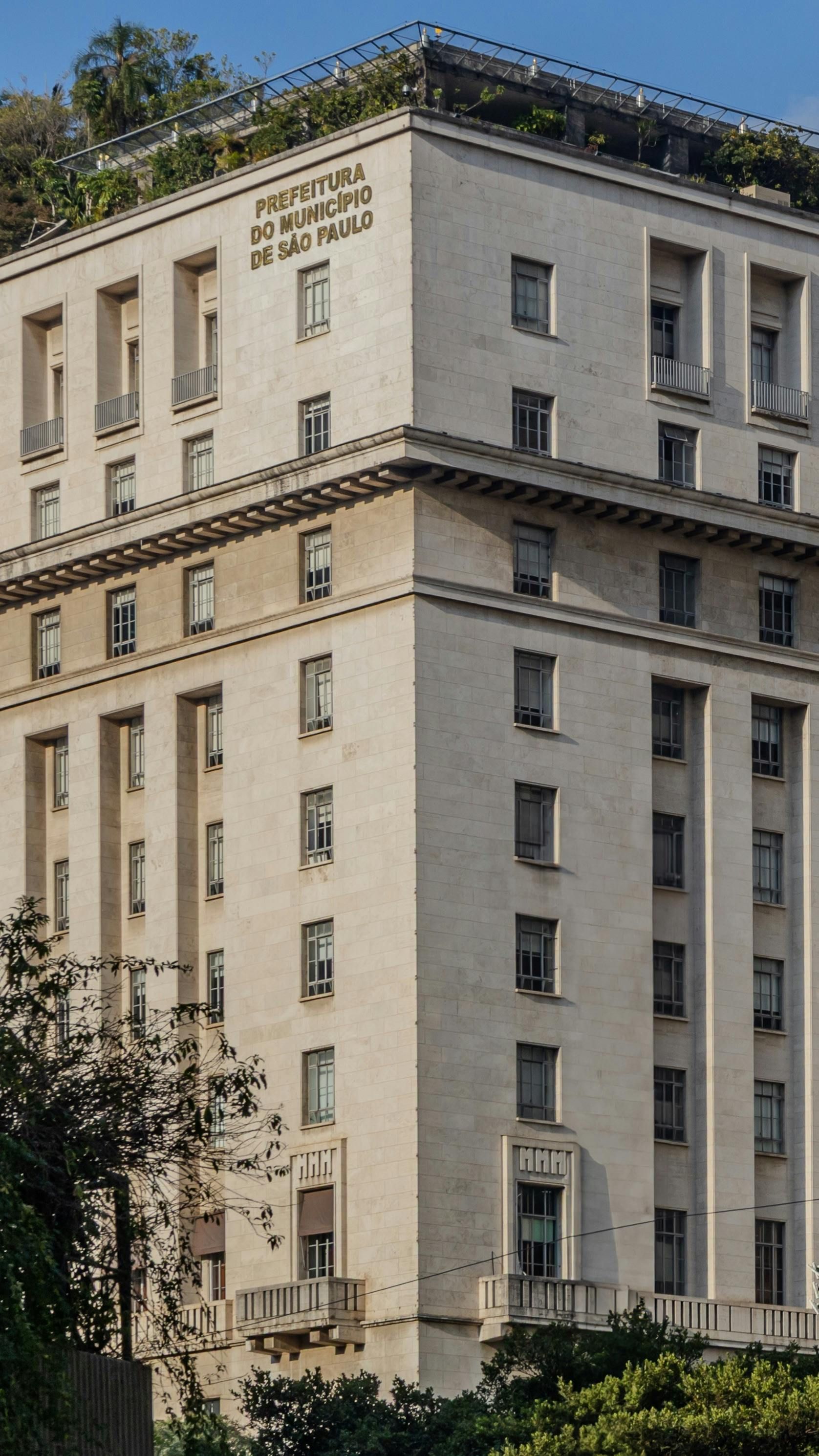 A tall, light-colored stone building with many windows and an inscription near the top, seen from a low angle.