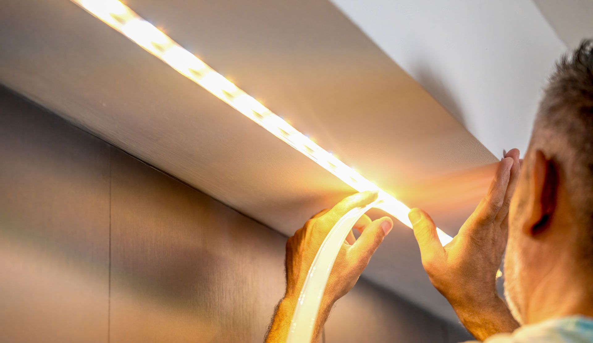 A person installs a glowing LED strip light into a recessed channel on a ceiling.