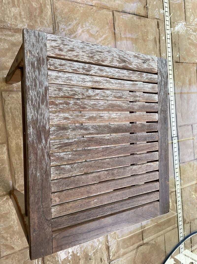 A wooden stool is sitting on a brick floor next to a brick wall.
