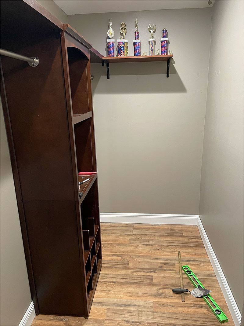 A walk in closet with wooden shelves and a shelf with trophies on it.