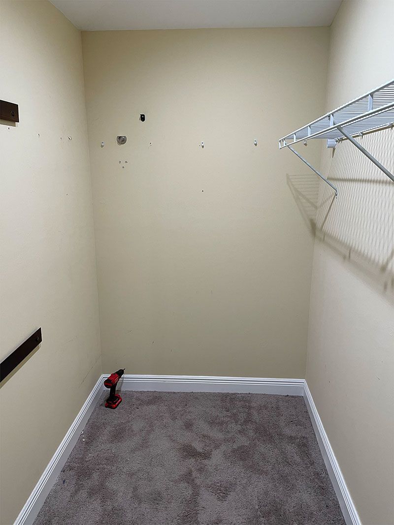 An empty closet with a drill on the floor.