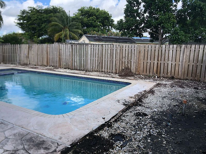 A wooden fence surrounds a swimming pool in a backyard