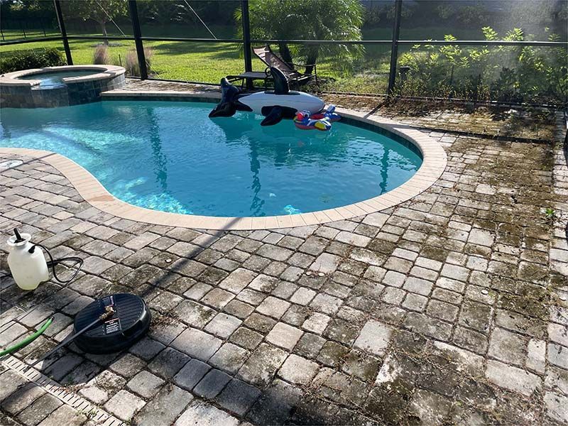 A swimming pool is surrounded by a brick patio and a screened in area.
