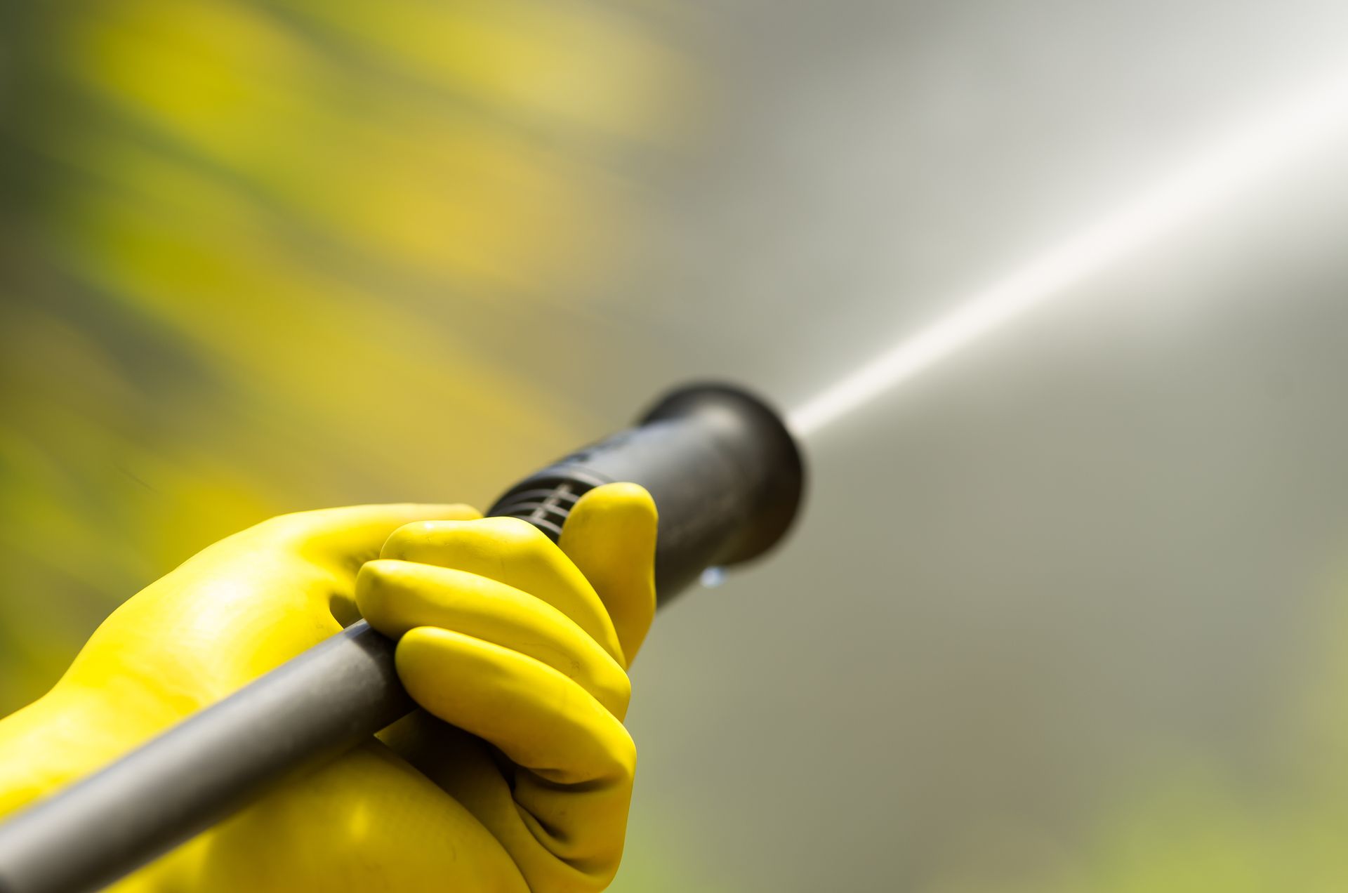 A person wearing yellow gloves is holding a high pressure washer.