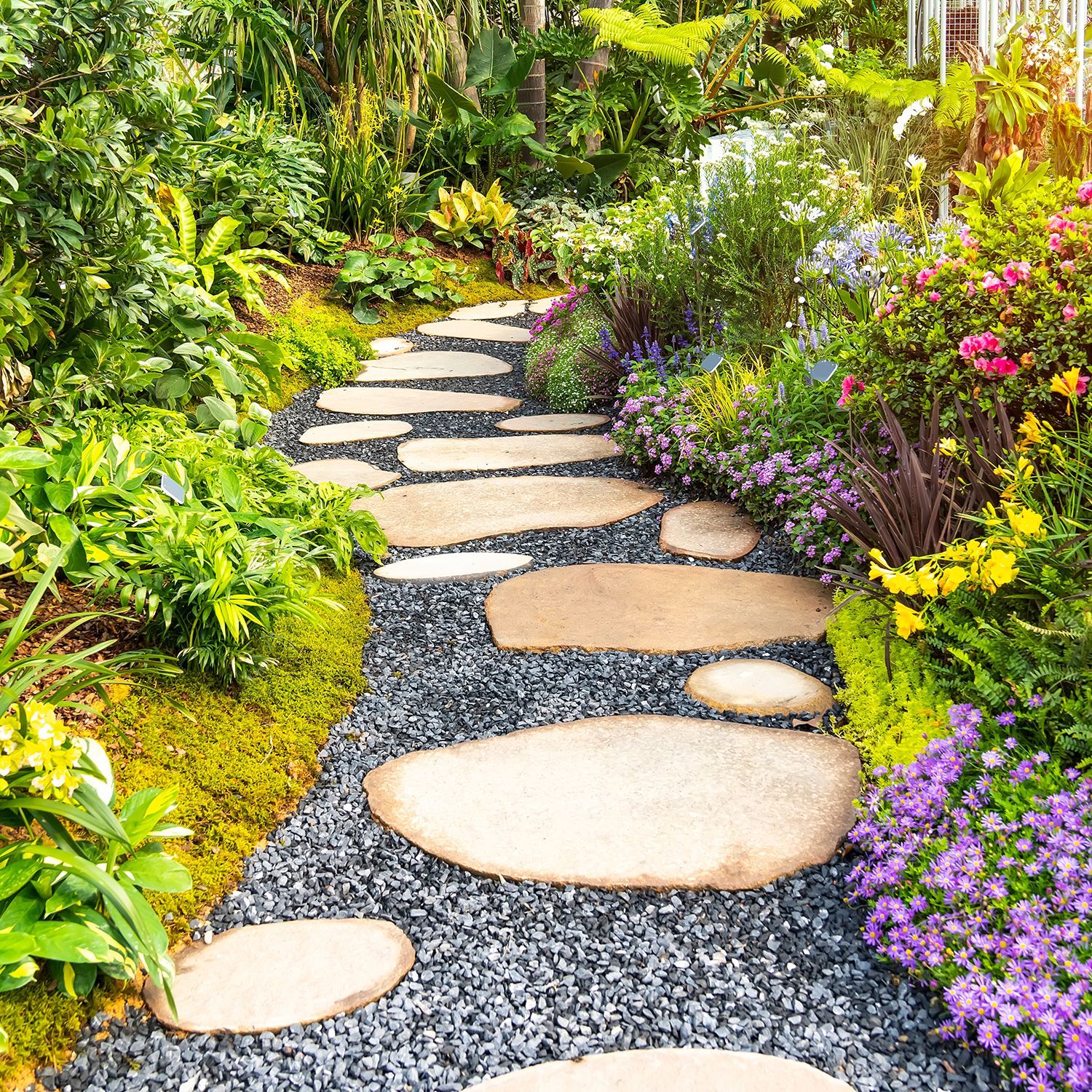 A stone path in a garden surrounded by flowers and plants.