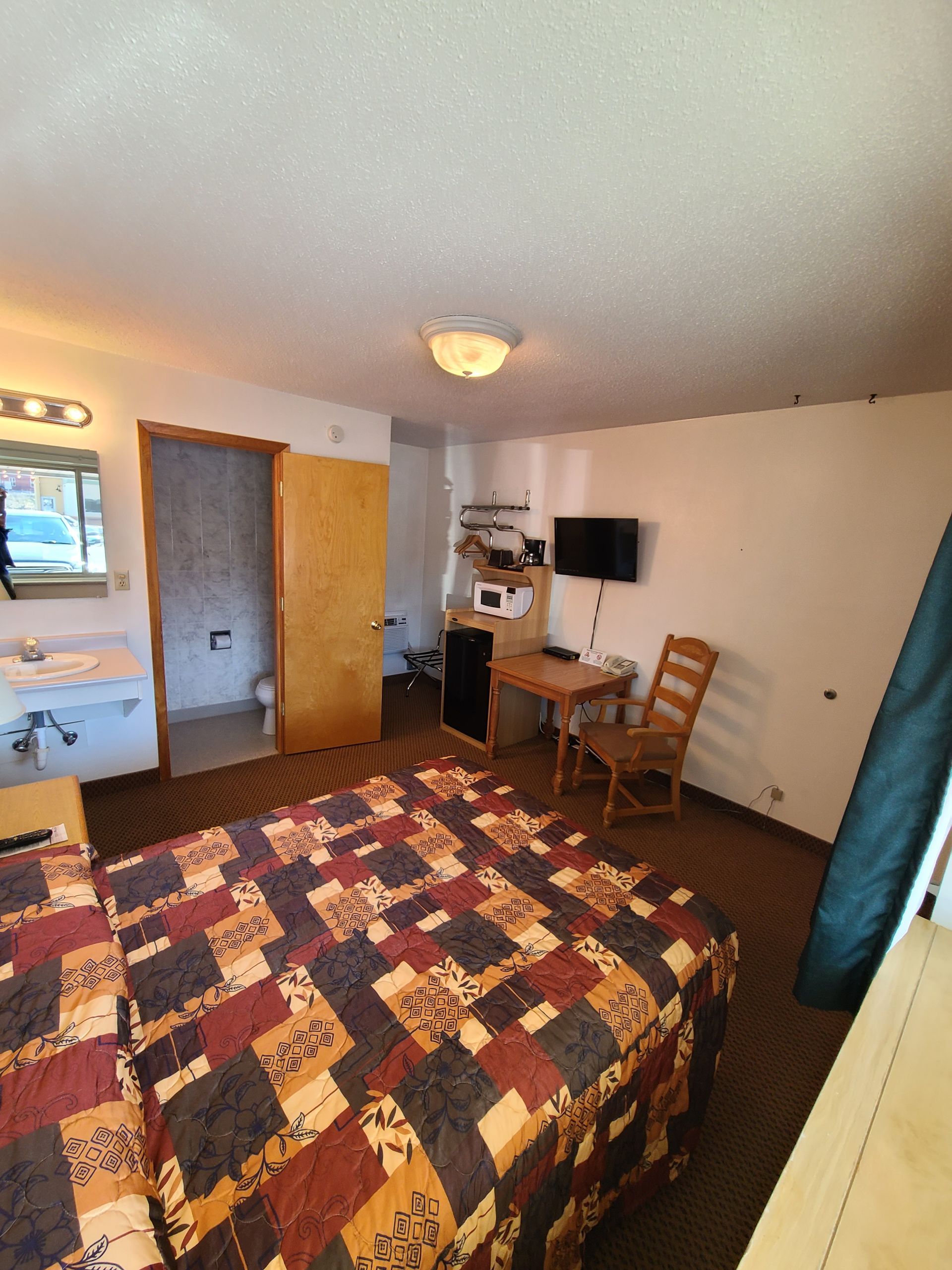 Motel room interior with bed, TV, microwave, desk, and bathroom.