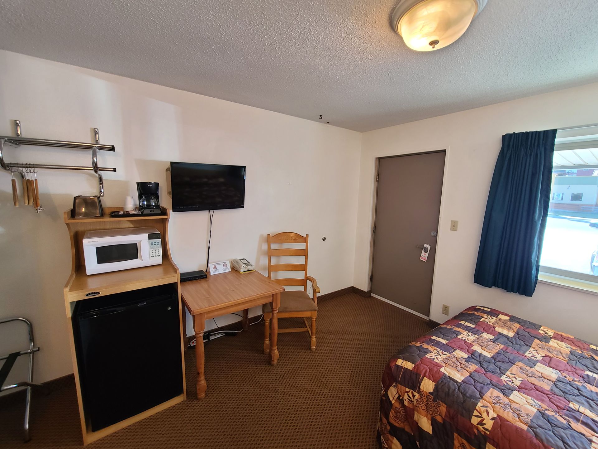 Small motel room with a bed, TV, microwave, desk, and a window with curtains.