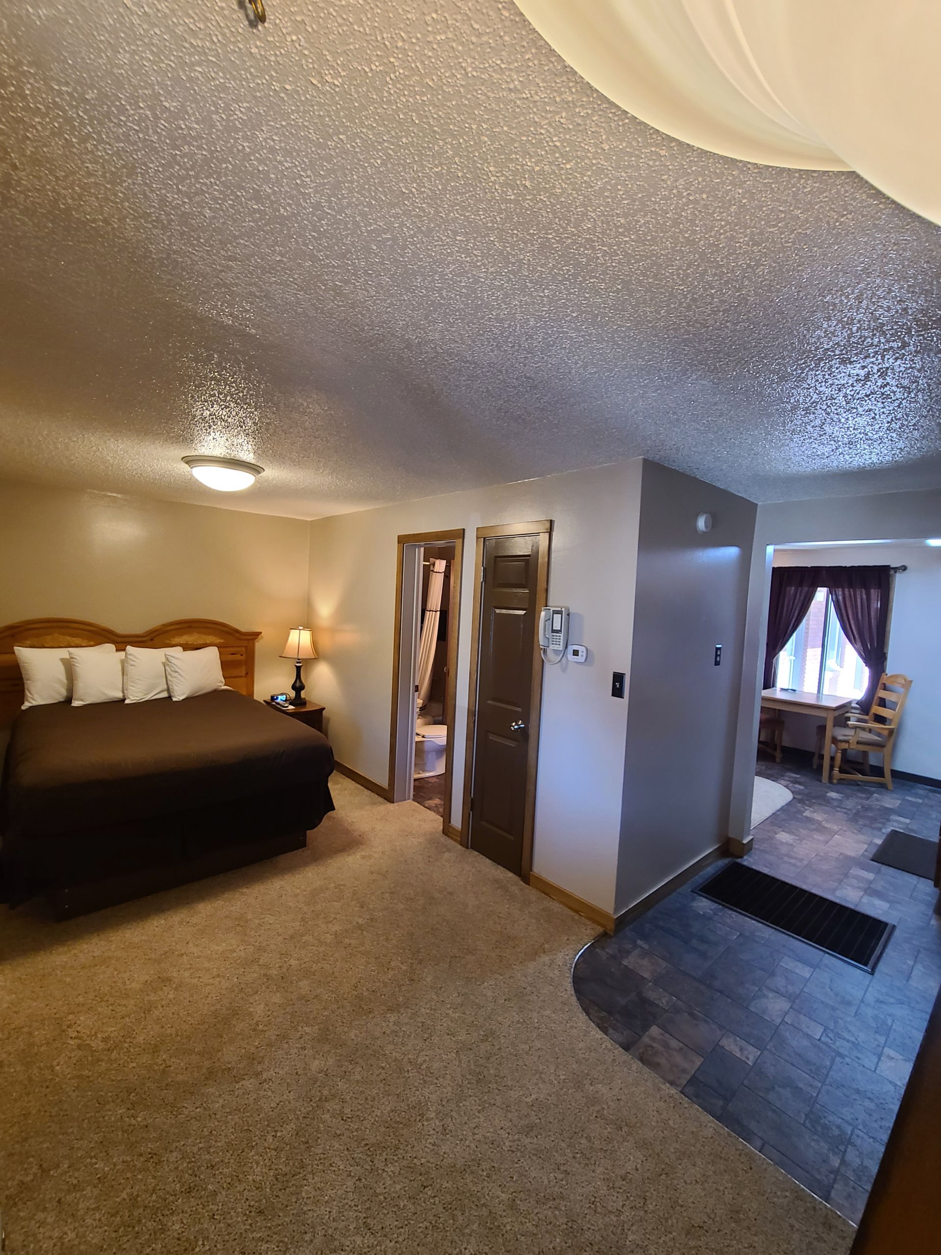 Bedroom with bed, doorway, small table, and carpeted floor. Brown and neutral colors.