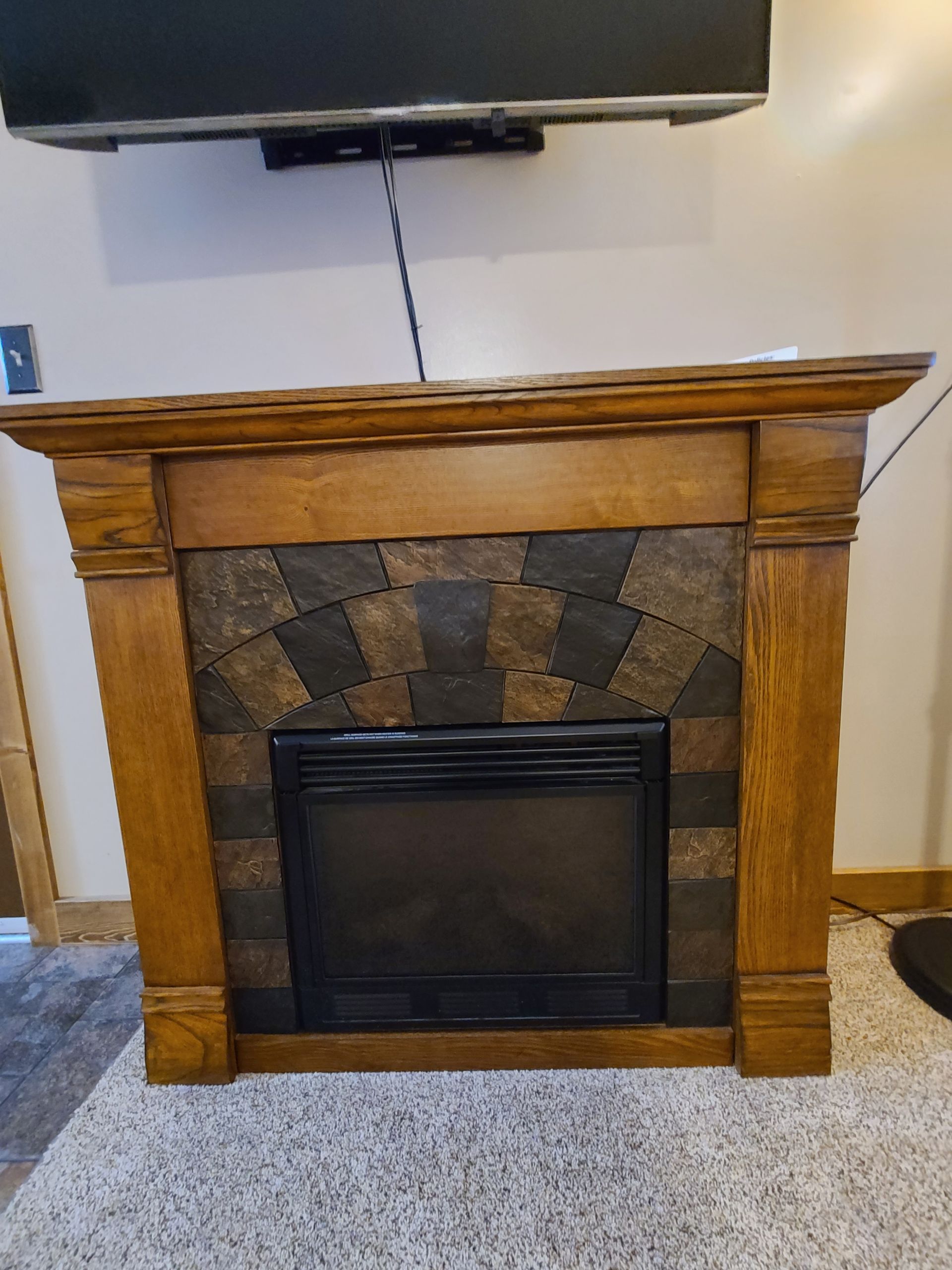 Wooden fireplace with dark stone tile and a black electric insert, beneath a mounted TV.