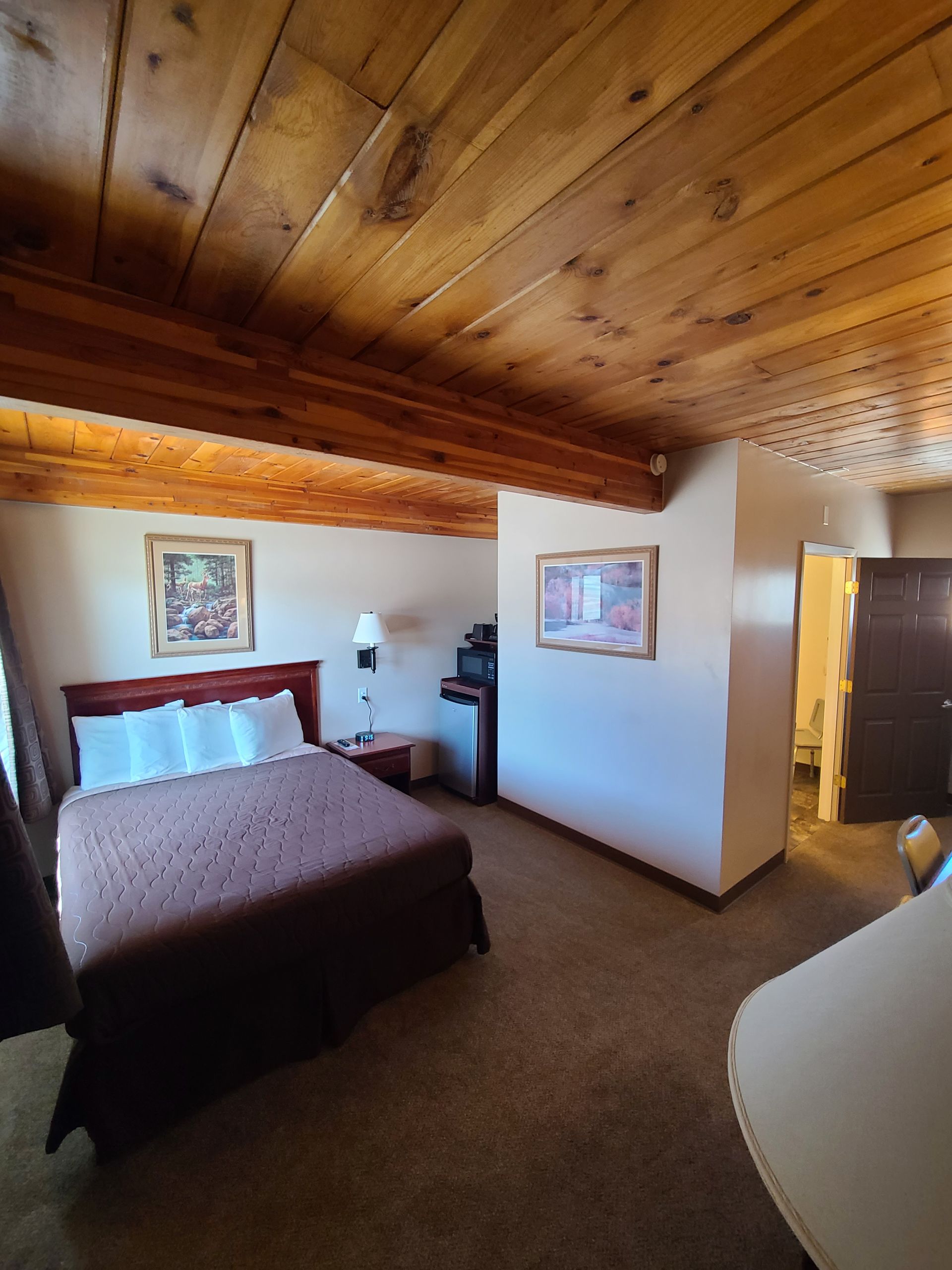 Bedroom with wooden ceiling, brown bedspread, artwork, television, and a doorway.