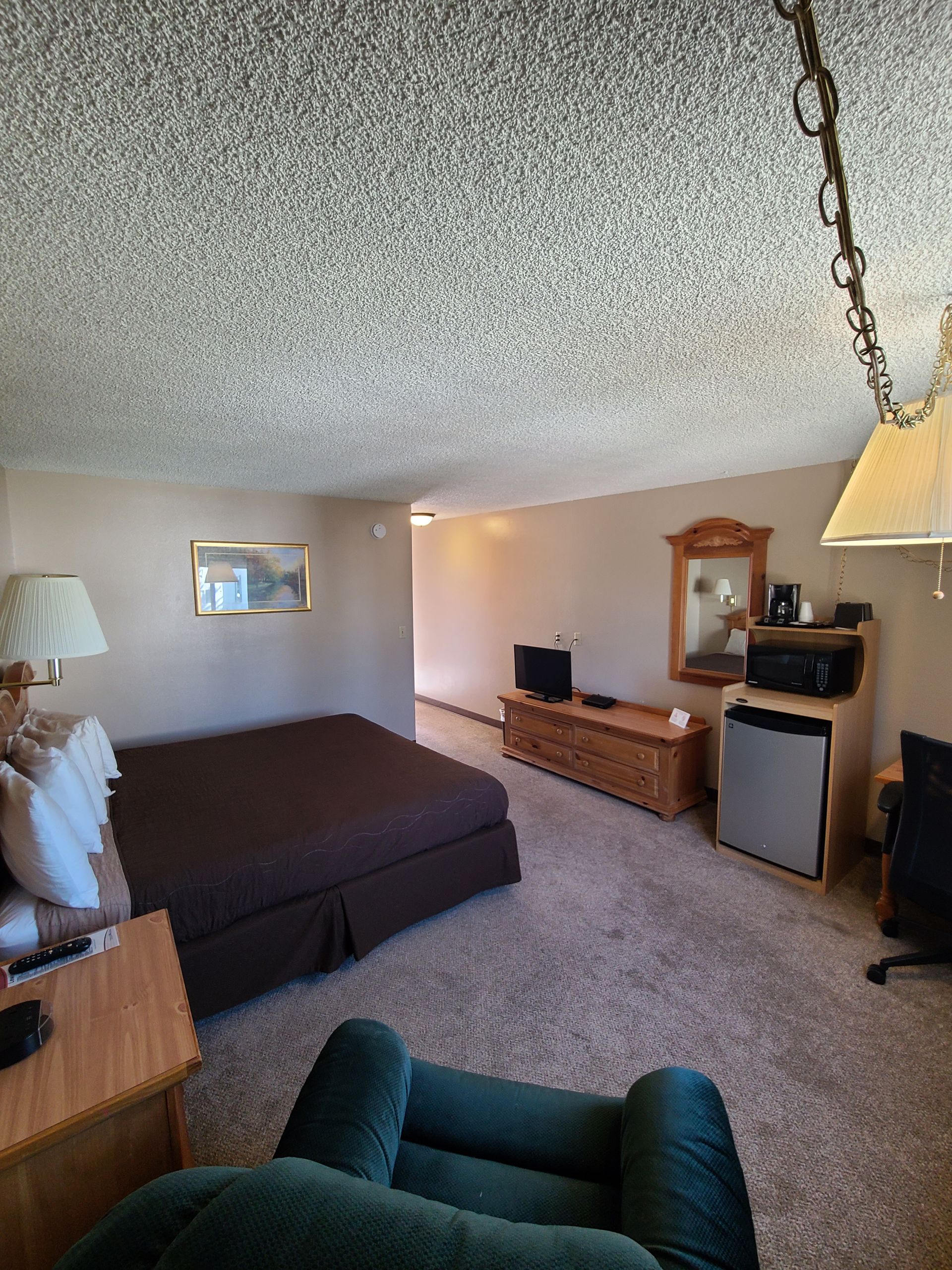 Hotel room with brown bed, beige walls, and a green armchair.