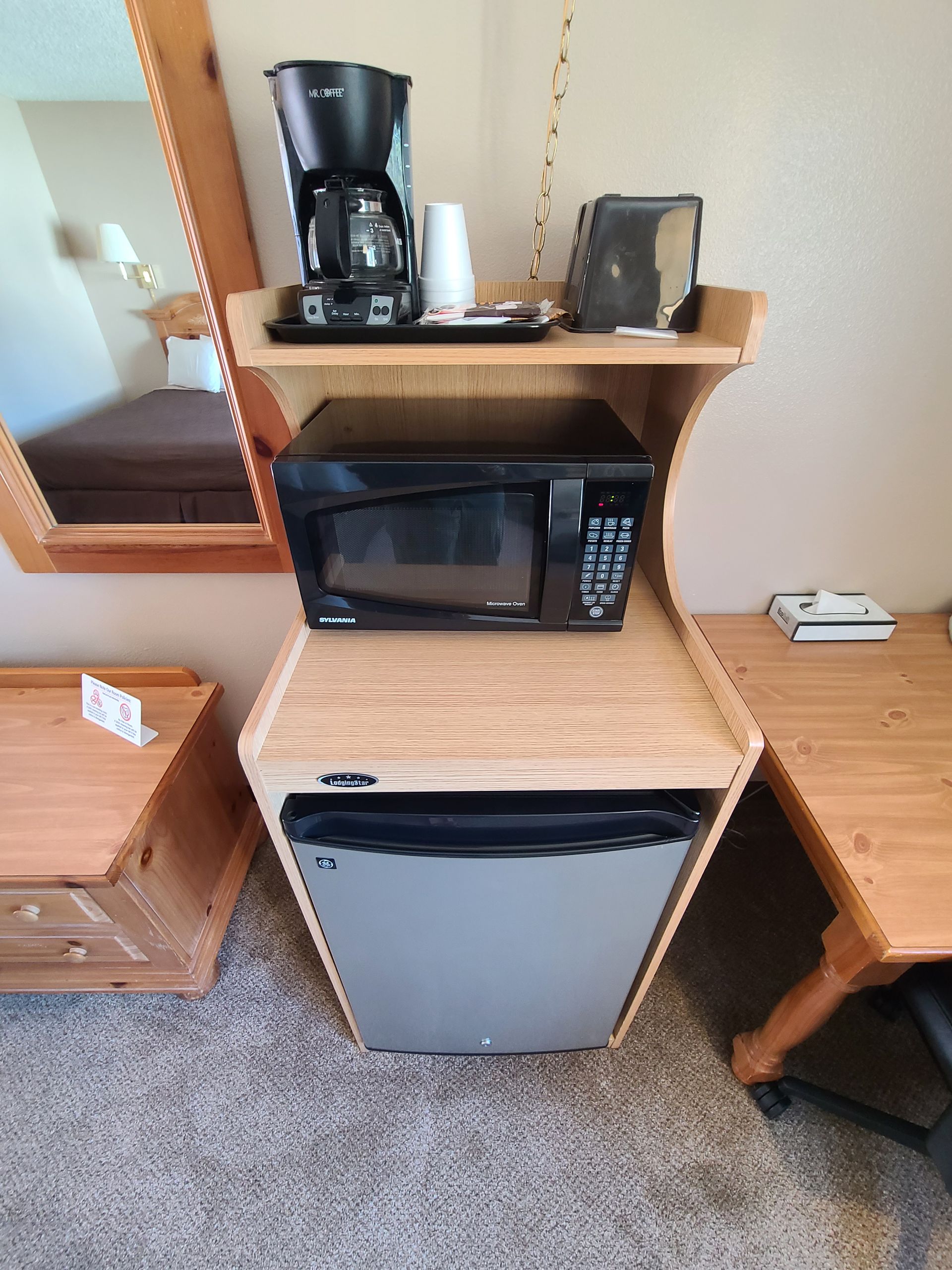 A hotel room kitchenette with microwave, refrigerator, coffee maker, and dresser.